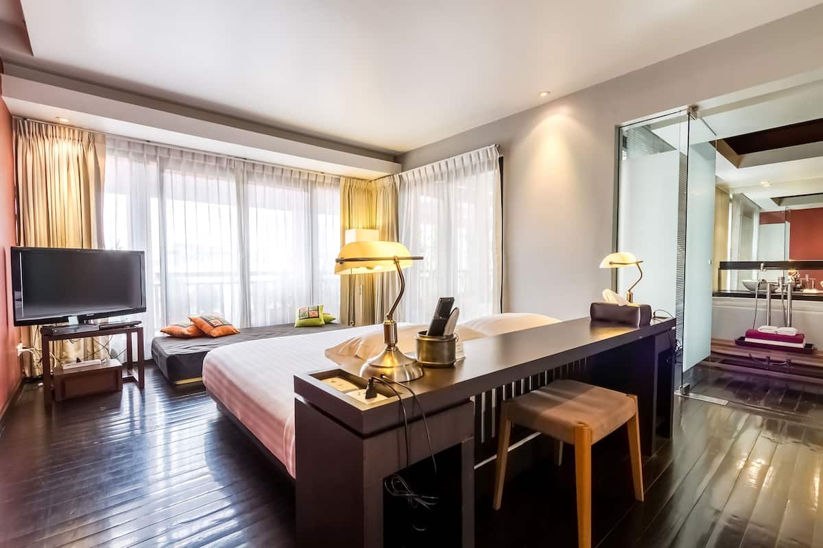 Una habitación de hotel moderna con una cama grande, un escritorio con lámpara, televisión y vistas a la ciudad a través de amplios ventanales.