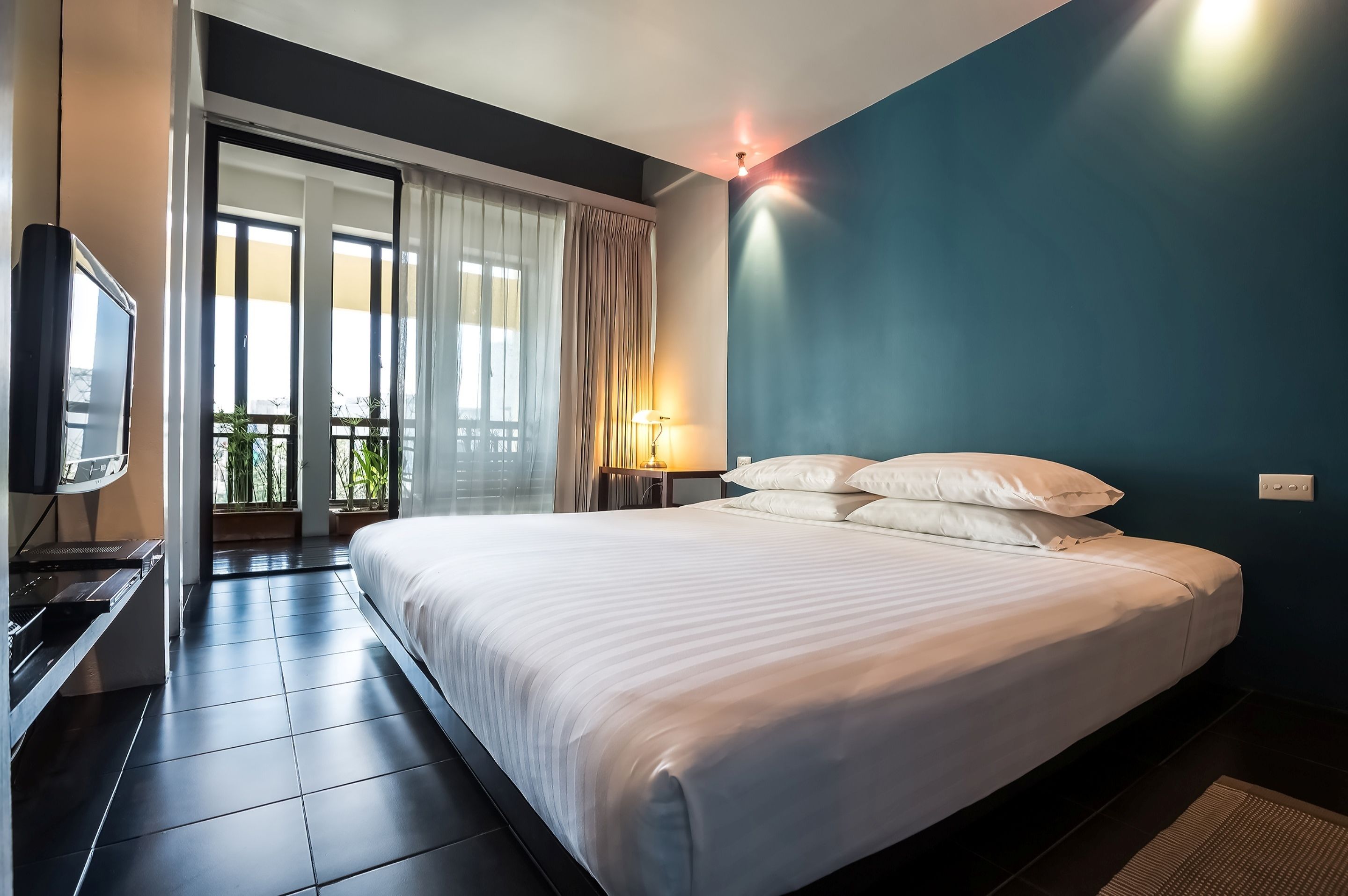 A hotel room with a bed, a TV, a lamp, and a view of the outdoors.