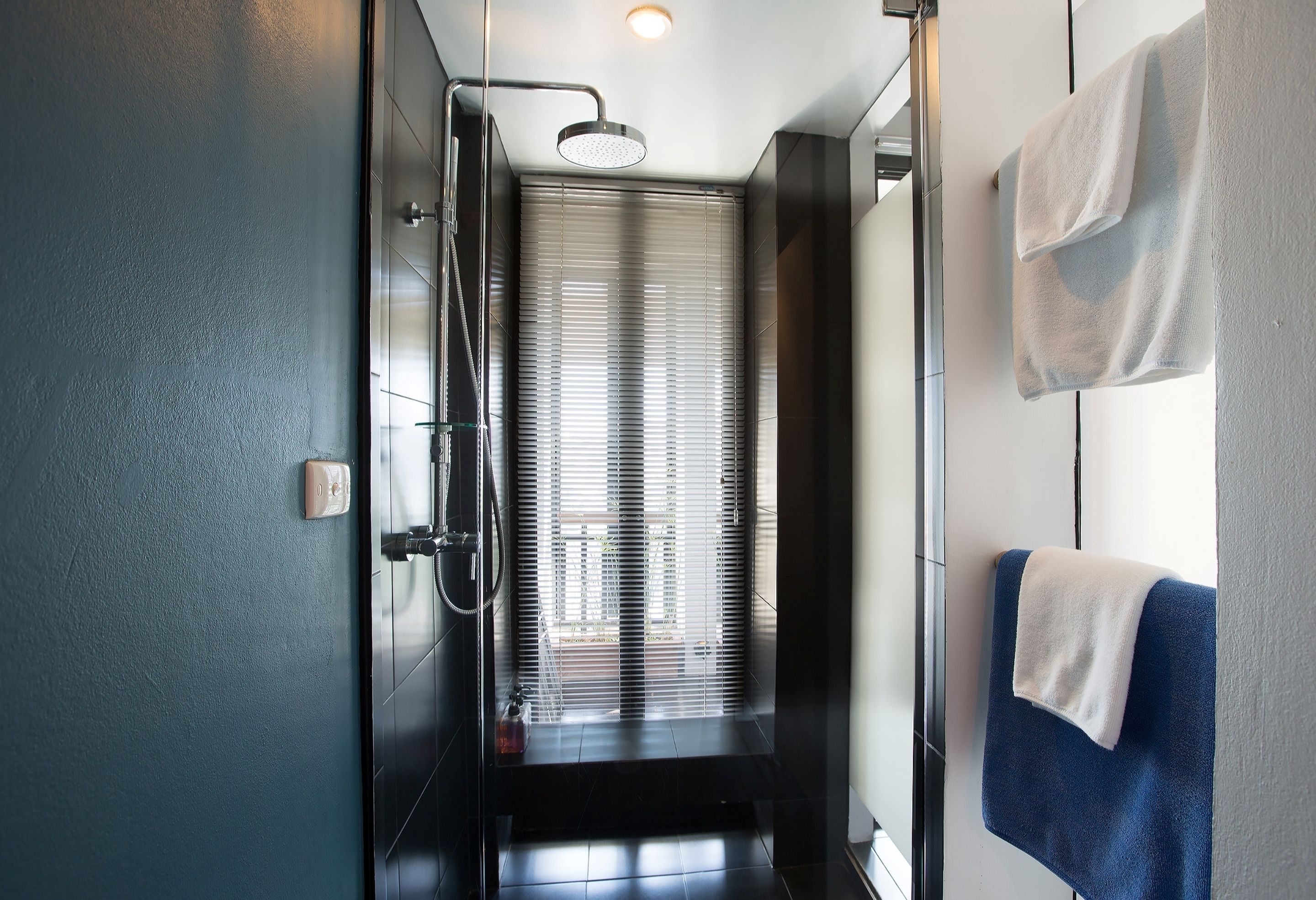 Een moderne badkamer met een glazen douchecabine, een handdoekrek met twee handdoeken, en een zichtbaar raam met zonwering.