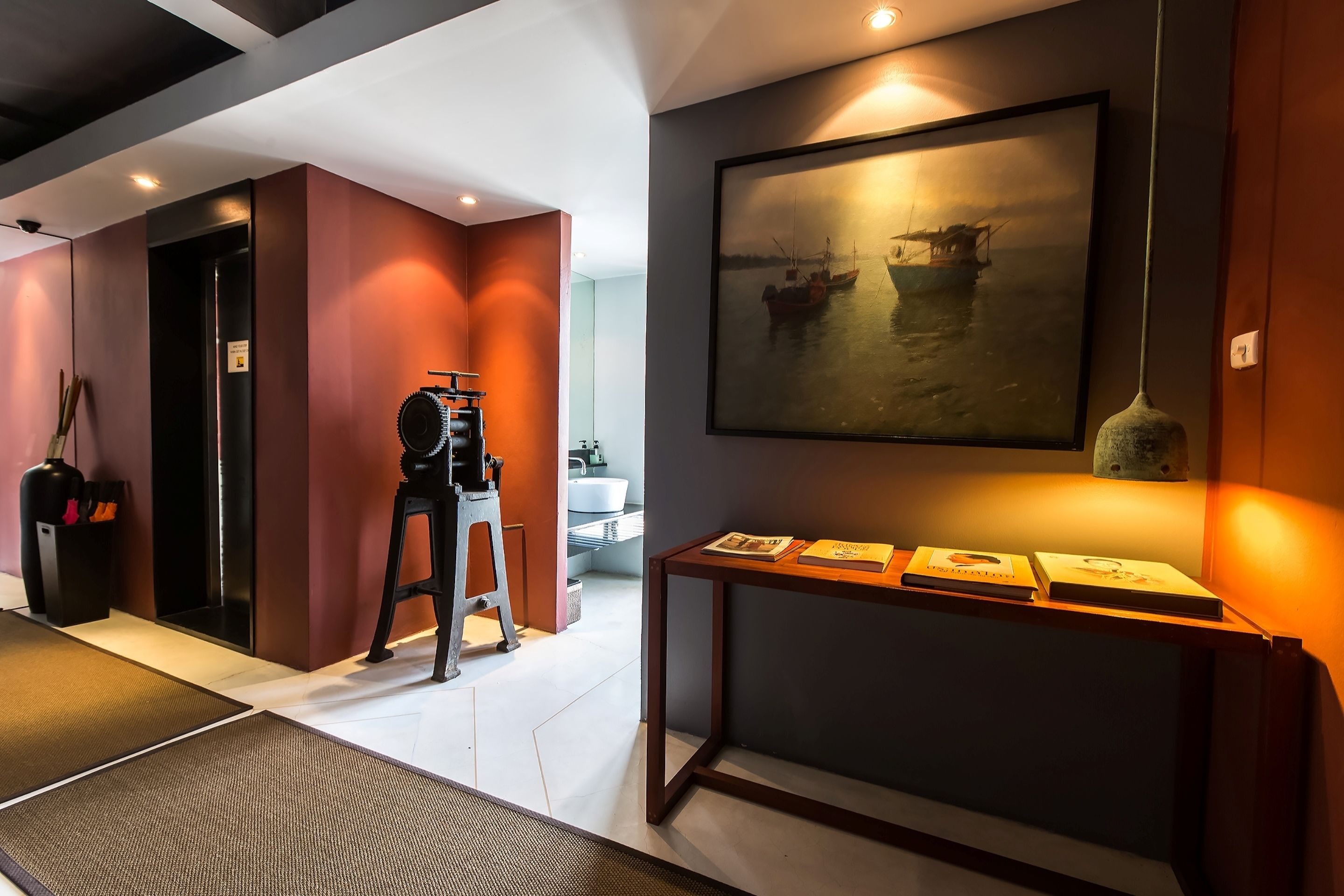 A modern hotel lobby with a large painting of boats on water, a reception desk, and a seating area.