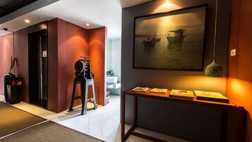 A modern hotel lobby with a large painting of boats on water, a reception desk, and a seating area.