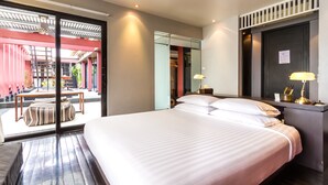 A modern hotel room with a large bed, a desk with a lamp, and a sliding glass door leading to an outdoor area with a pool and seating. - LoogChoob Homestay (Bangkok)