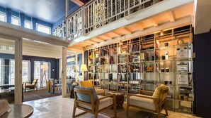 A spacious reading area with comfortable seating, a large bookshelf, and a balcony with a railing. - LoogChoob Homestay (Bangkok)