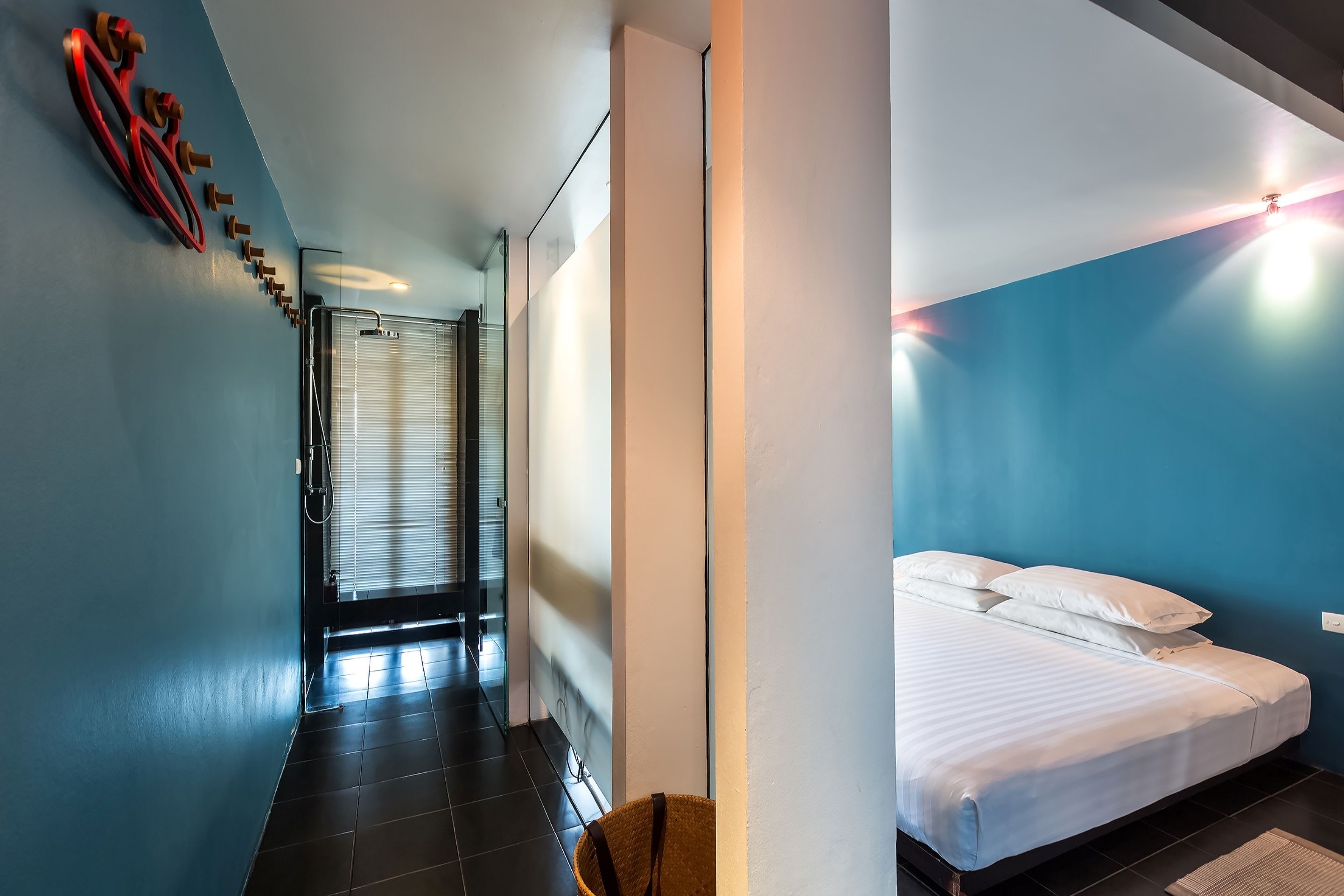 A modern hotel room with a bed, a wall-mounted light, and a hallway leading to a bathroom.