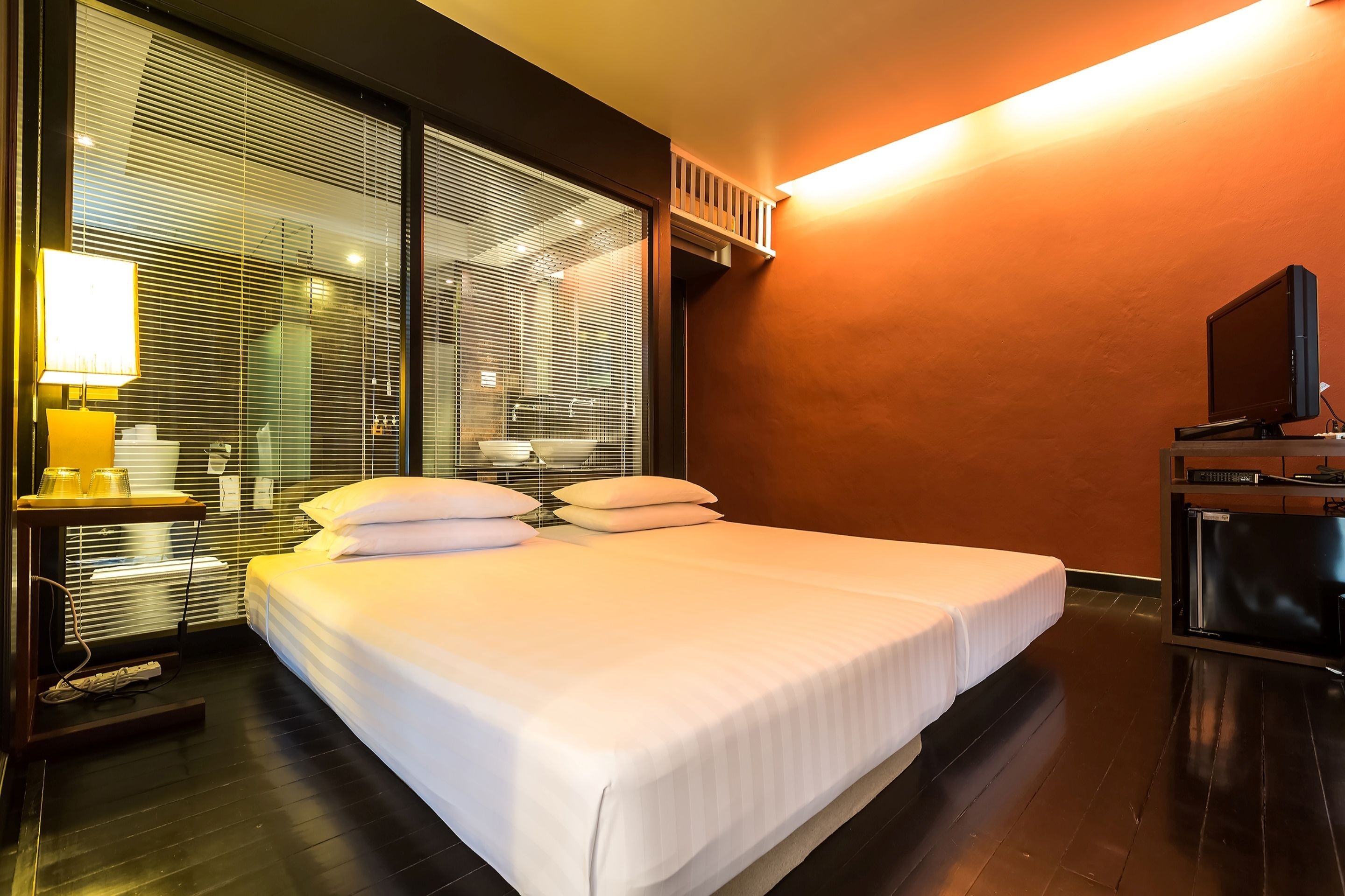A hotel room with a large bed, a bedside table with a lamp, a television, and a window with blinds.