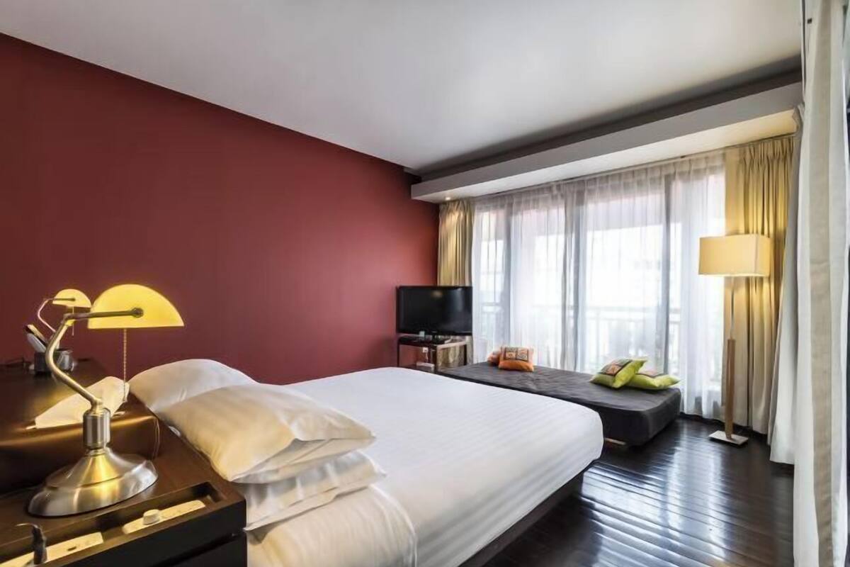 Una habitación de hotel con una cama grande, un escritorio con lámpara, televisión y ventana con cortinas.