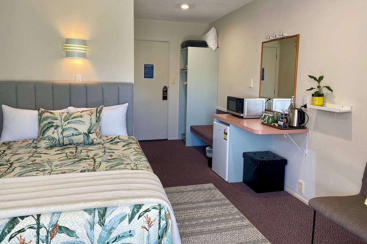 A hotel room with a bed, bedside table, microwave, and a small kitchenette.