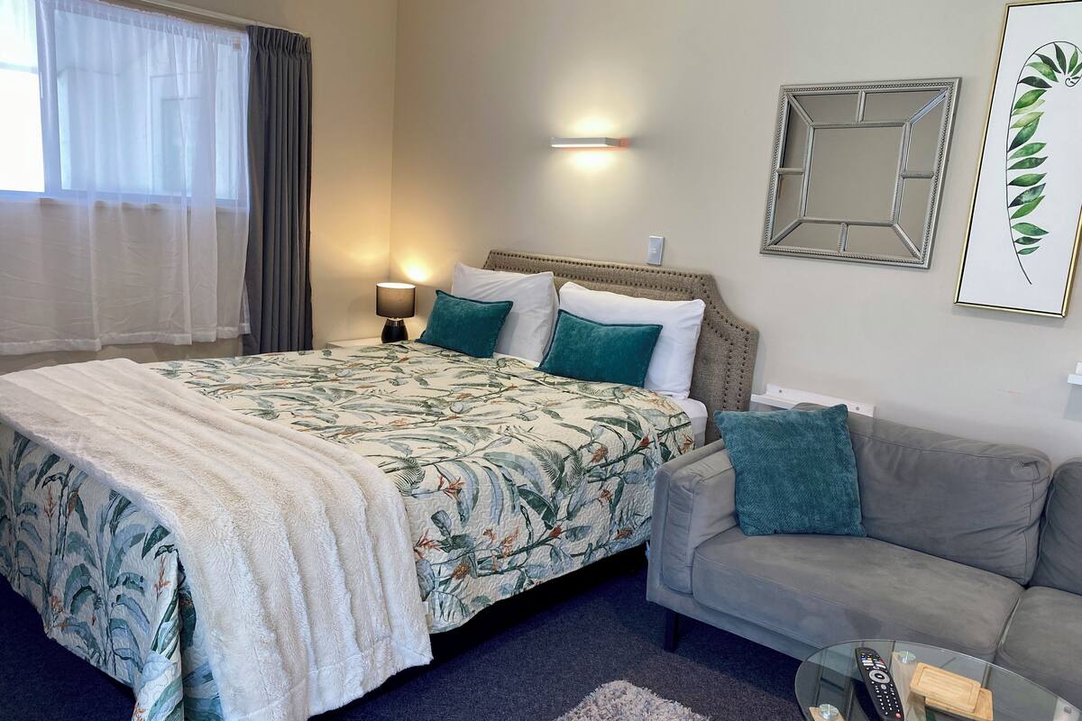 A neatly arranged bedroom with a bed, a sofa, a glass coffee table, and a wall-mounted lamp.