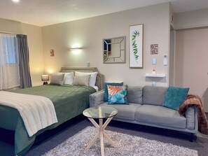 Una habitación de hotel con una cama, un sofá, una mesita de cristal y una mesita auxiliar.