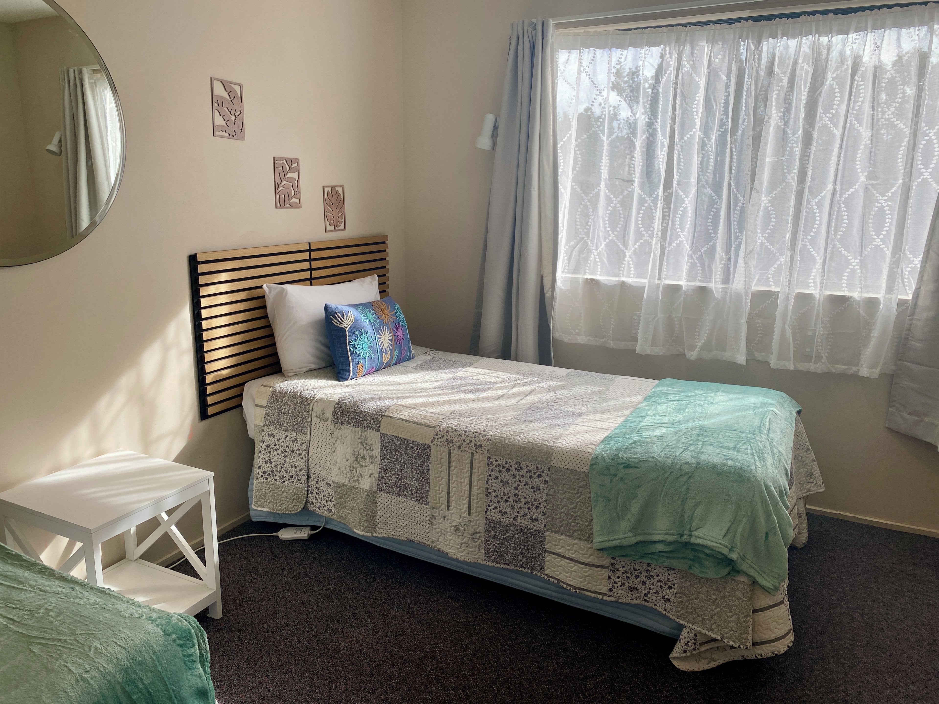A bedroom with a bed, a bedside table, a mirror, and a window with curtains.