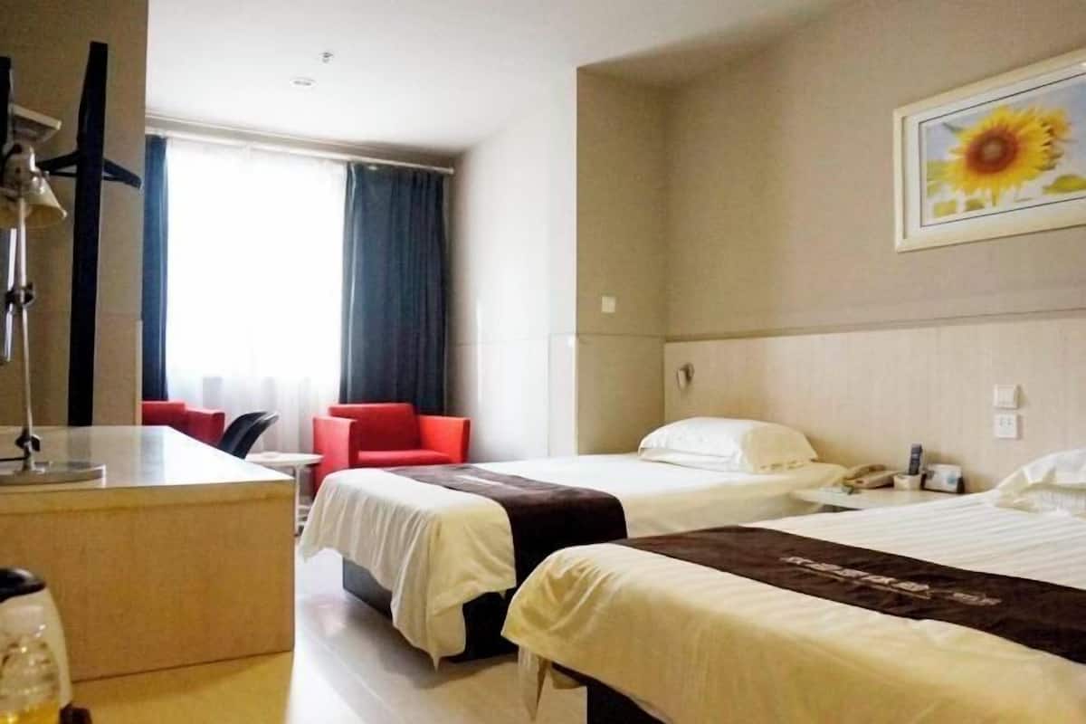 A hotel room with two beds, a desk, a chair, and a window with curtains.