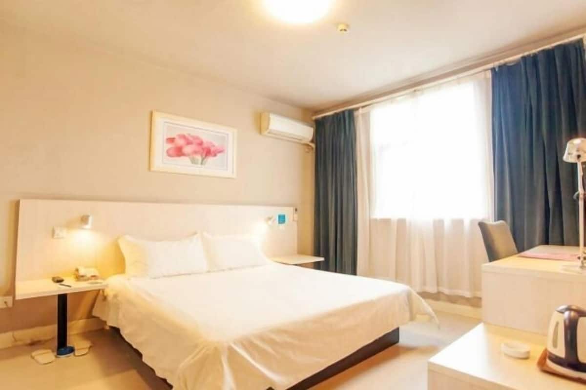 A hotel room with a bed, bedside table, lamp, and a window with curtains.