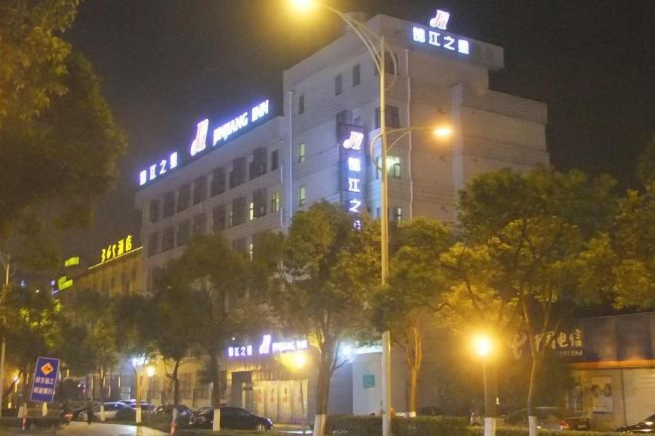 Un immeuble à plusieurs étages, doté d’une enseigne lumineuse, probablement un hôtel ou un immeuble commercial, avec des arbres à l’avant et des lampadaires le long du trottoir.