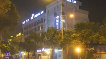 A multi-story building with illuminated signage, likely a hotel or commercial property, with trees in front and street lamps along the sidewalk.