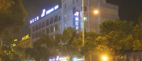 A multi-story building with illuminated signage, likely a hotel or commercial property, with trees in front and street lamps along the sidewalk.
