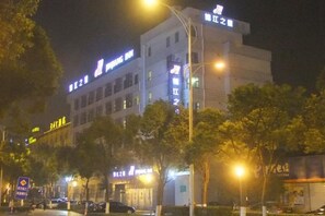 Un immeuble à plusieurs étages, doté d’une enseigne lumineuse, probablement un hôtel ou un immeuble commercial, avec des arbres à l’avant et des lampadaires le long du trottoir.
