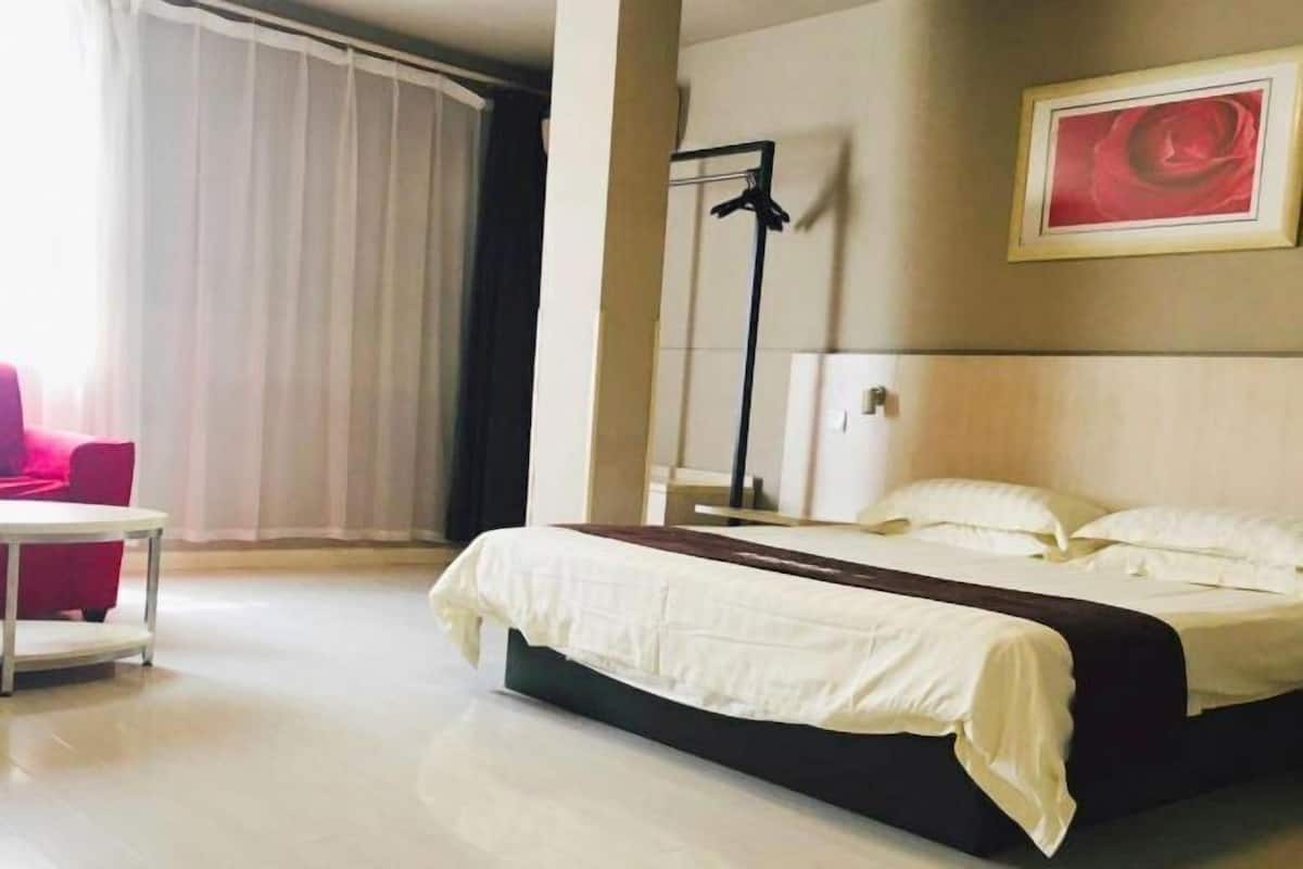 A hotel room with a bed, a chair, a table, and a painting on the wall.
