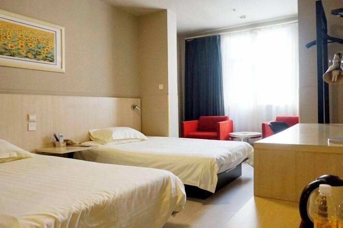 A hotel room with two beds, a desk, a chair, and a painting on the wall.