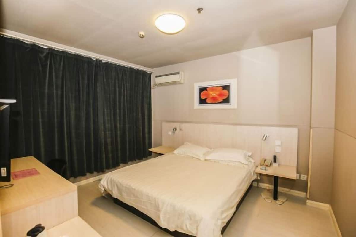 A hotel room with a bed, bedside tables, a desk, an air conditioning unit, and a picture on the wall.
