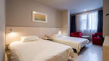 A hotel room with two beds, a small table, a red chair, and a painting on the wall.