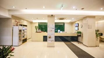A hotel reception area with a reception desk, a plant, and a clock on the wall.