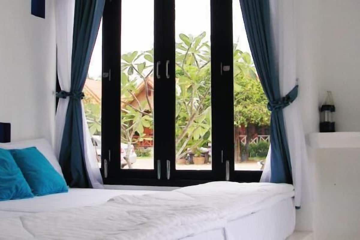 Un dormitorio con cama, cortinas y vistas al verde exterior.