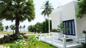 A white building with a blue door, surrounded by lush greenery and palm trees. - Laemsing Whitehouse Resort (Laem Sing)