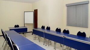 Un salón de conferencias con una larga mesa, sillas, una pizarra y un ventanal con persianas.