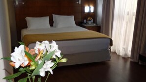 Una habitación de hotel con una cama grande, una mesita de noche, una lámpara y un florero con flores.
