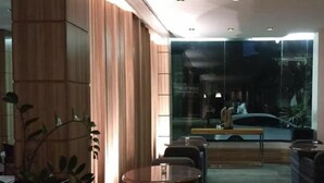 Un espacio interior moderno con paneles de madera, una pared de cristal y una zona de estar con mesas y sillas.