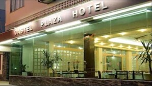 Exterior de un hotel con fachada de vidrio, un cartel que dice "Castel Plaza Hotel" y una entrada visible.