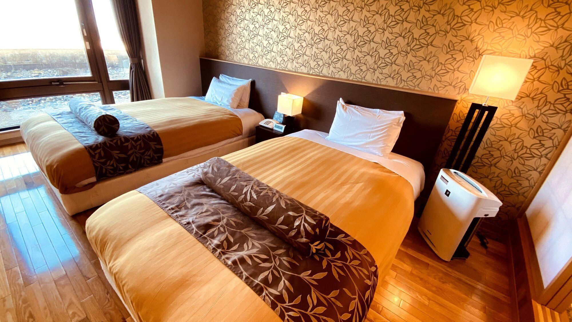 Une chambre d’hôtel avec deux lits, une table de chevet avec une lampe, un téléphone et une poubelle.