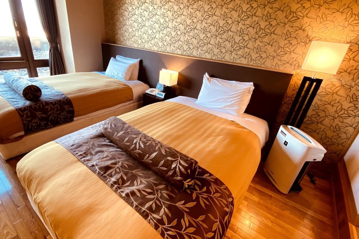 Ein Hotelzimmer mit zwei Betten, einem Nachttisch mit Lampe, einem Telefon und einem Mülleimer.