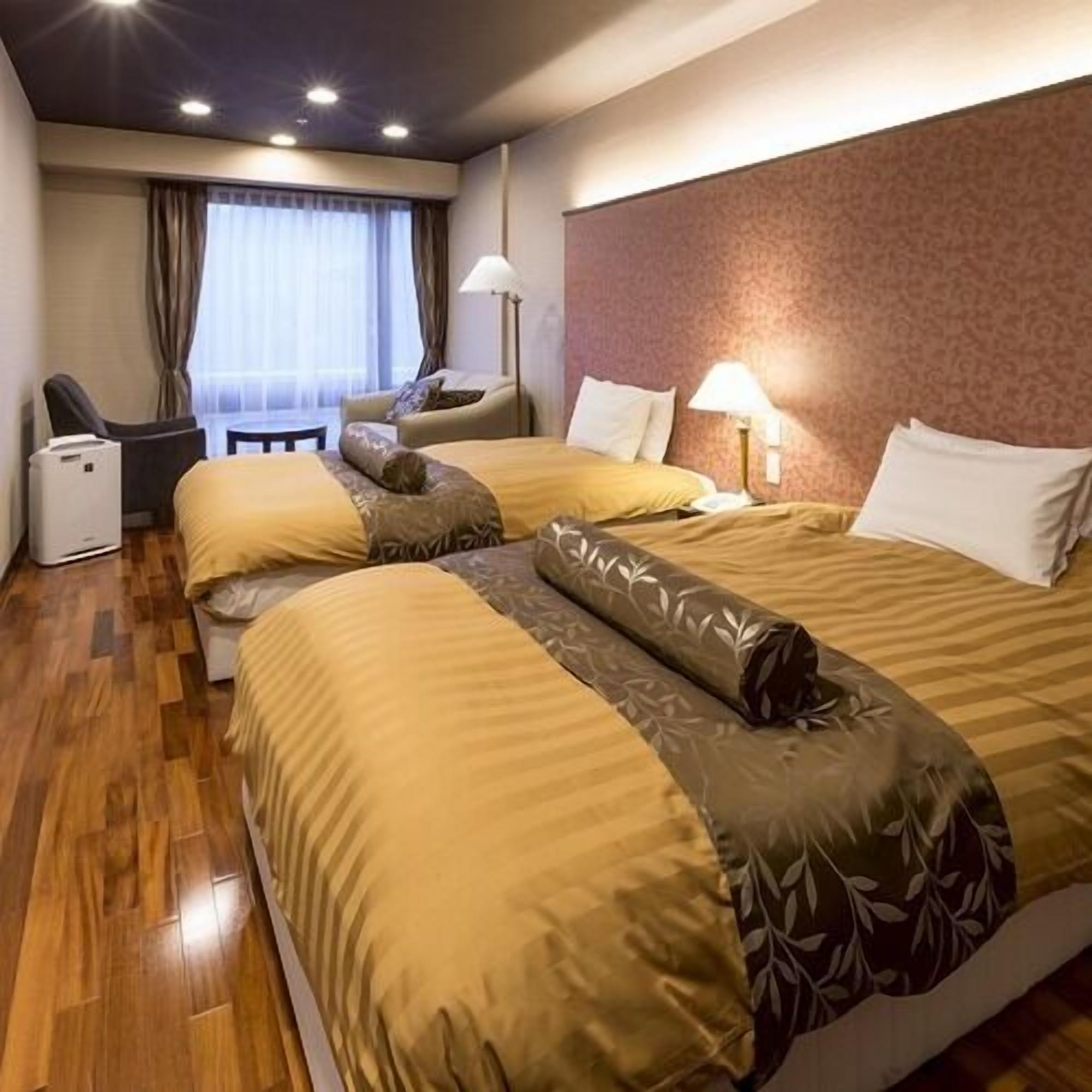 Une chambre d’hôtel avec deux lits, un bureau, une chaise, une lampe et une fenêtre avec des rideaux.