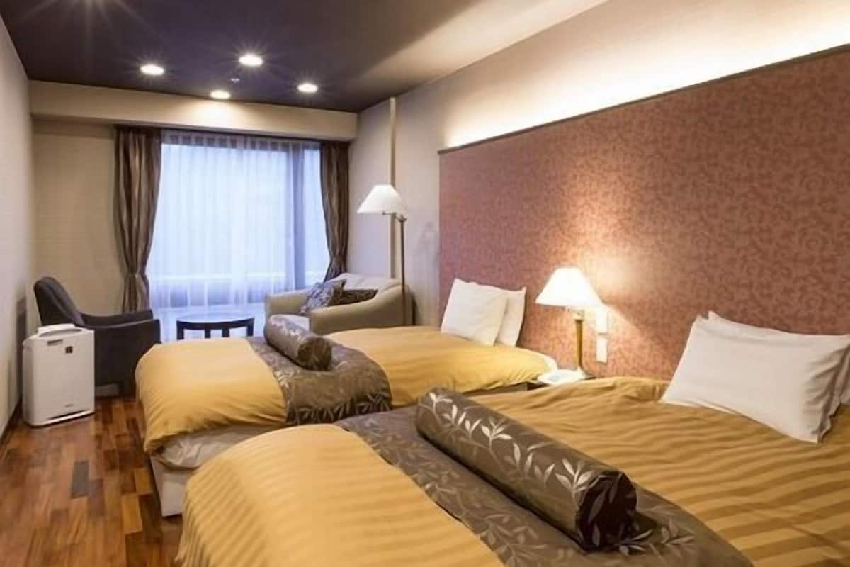 Ein Hotelzimmer mit zwei Betten, einem Schreibtisch, einem Stuhl, einer Lampe und einem Fenster mit Vorhängen.