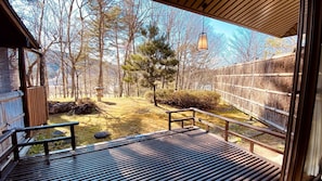 A wooden deck with a bench, a stone lantern, and a bamboo fence in a forested area.