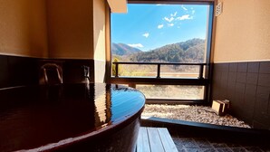 A bathroom with a large bathtub, a window with a mountain view, and a wooden bench. - Hotel Mori no Kaze Oshuku (Shizukuishi)