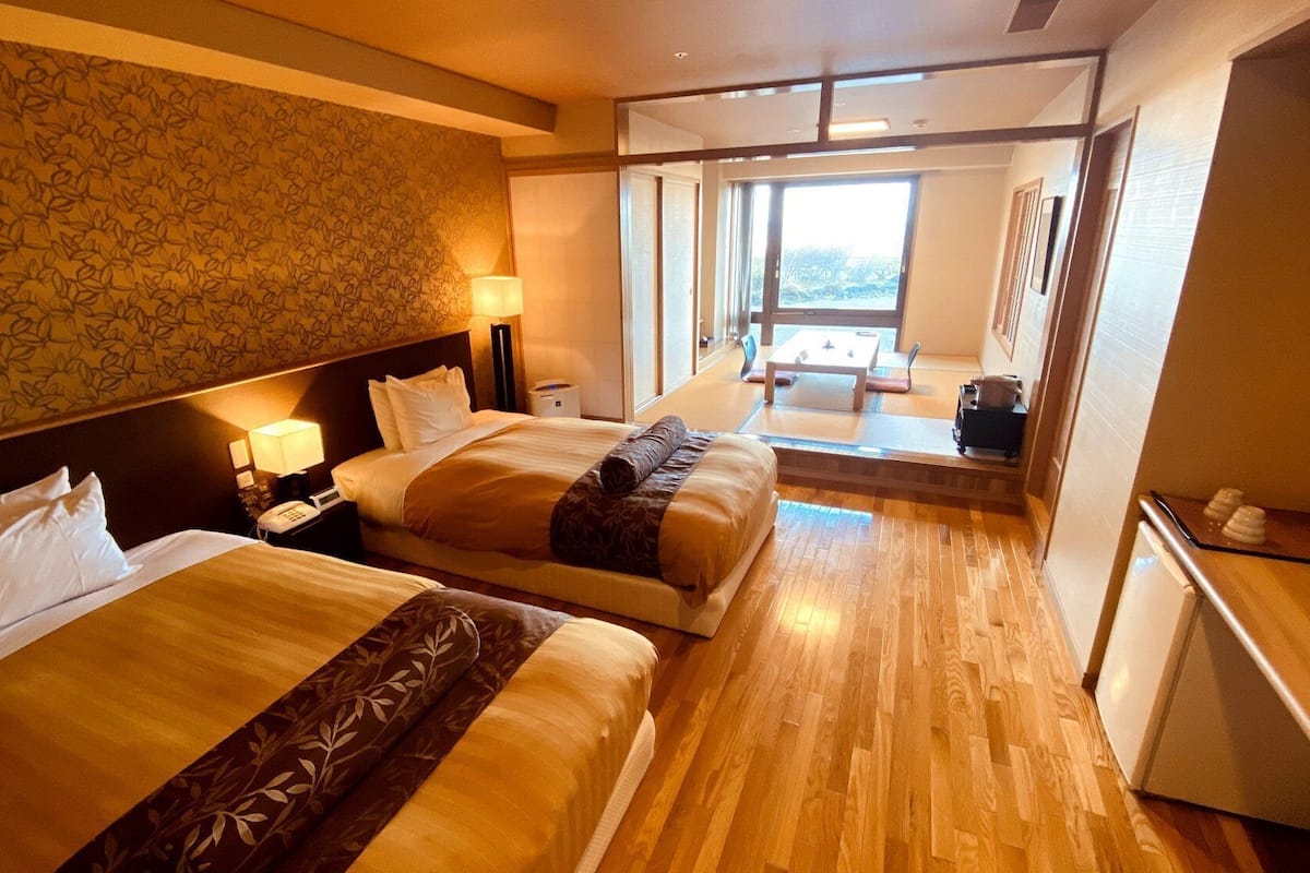 Ein Hotelzimmer mit zwei Betten, einem Schreibtisch, einem Stuhl und Blick ins Freie.