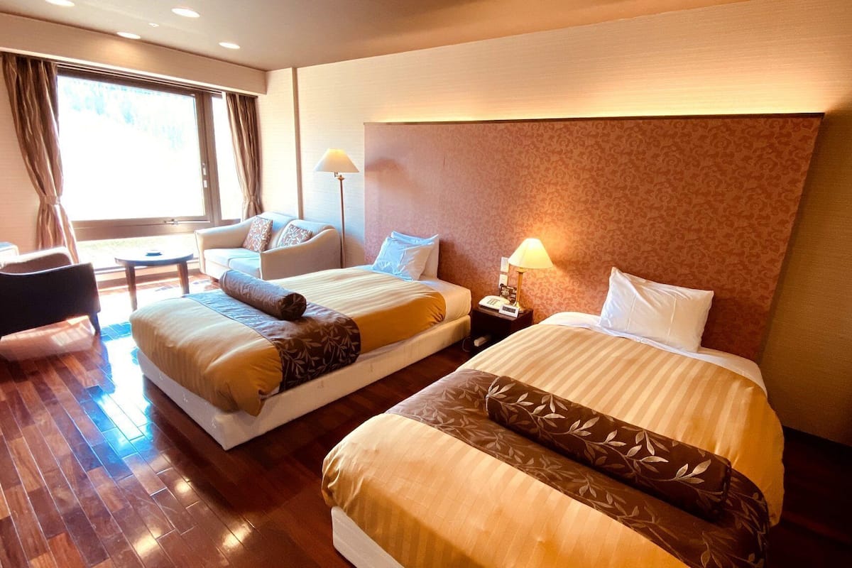 Ein Hotelzimmer mit zwei Betten, einem Sofa, einem Sessel, einem kleinen Tisch und einer Lampe.
