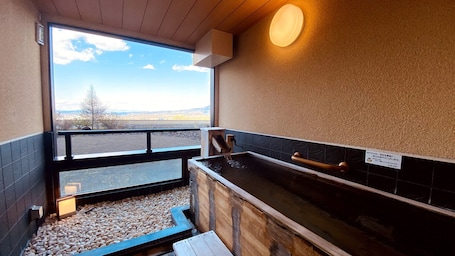 A sauna room with a wooden bench, a black tiled wall, and a window offering a view of the outdoors.