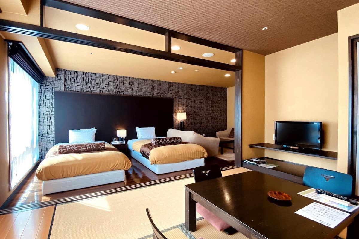 Ein modernes Hotelzimmer mit zwei Betten, einem Fernseher, einem Schreibtisch und Blick auf die Stadt.