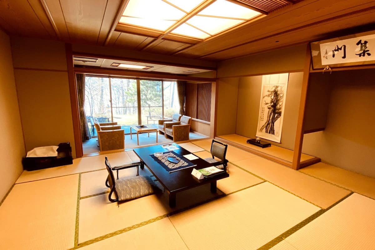 Ein traditioneller japanischer Raum mit Tatami-Boden, einem niedrigen Tisch mit Tee-Set, einer Couch und einem großen Fenster.