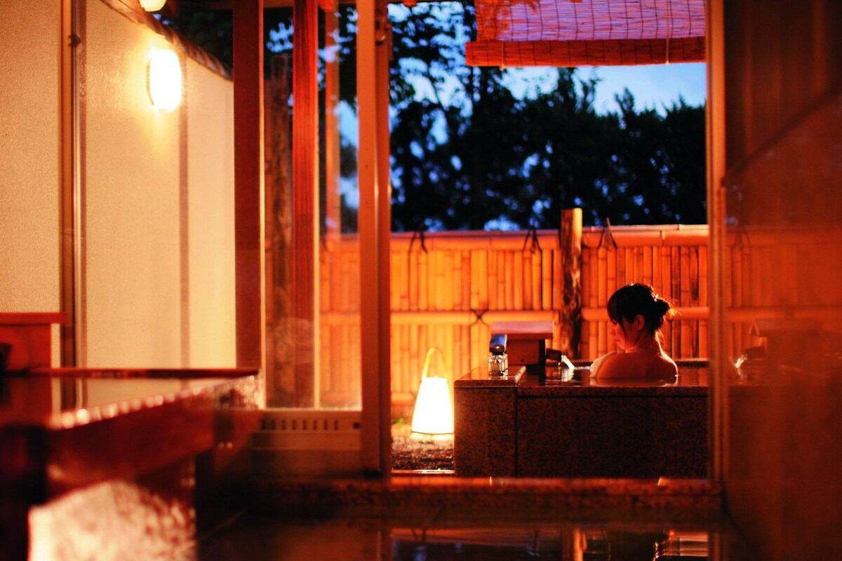 Un onsen japonés tradicional con interior de madera y vista al cielo nocturno.