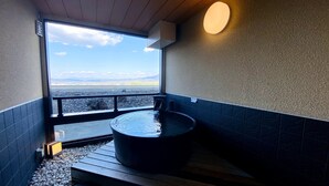 A hot tub in a room with a view of a body of water and mountains. - Hotel Mori no Kaze Oshuku (Shizukuishi)