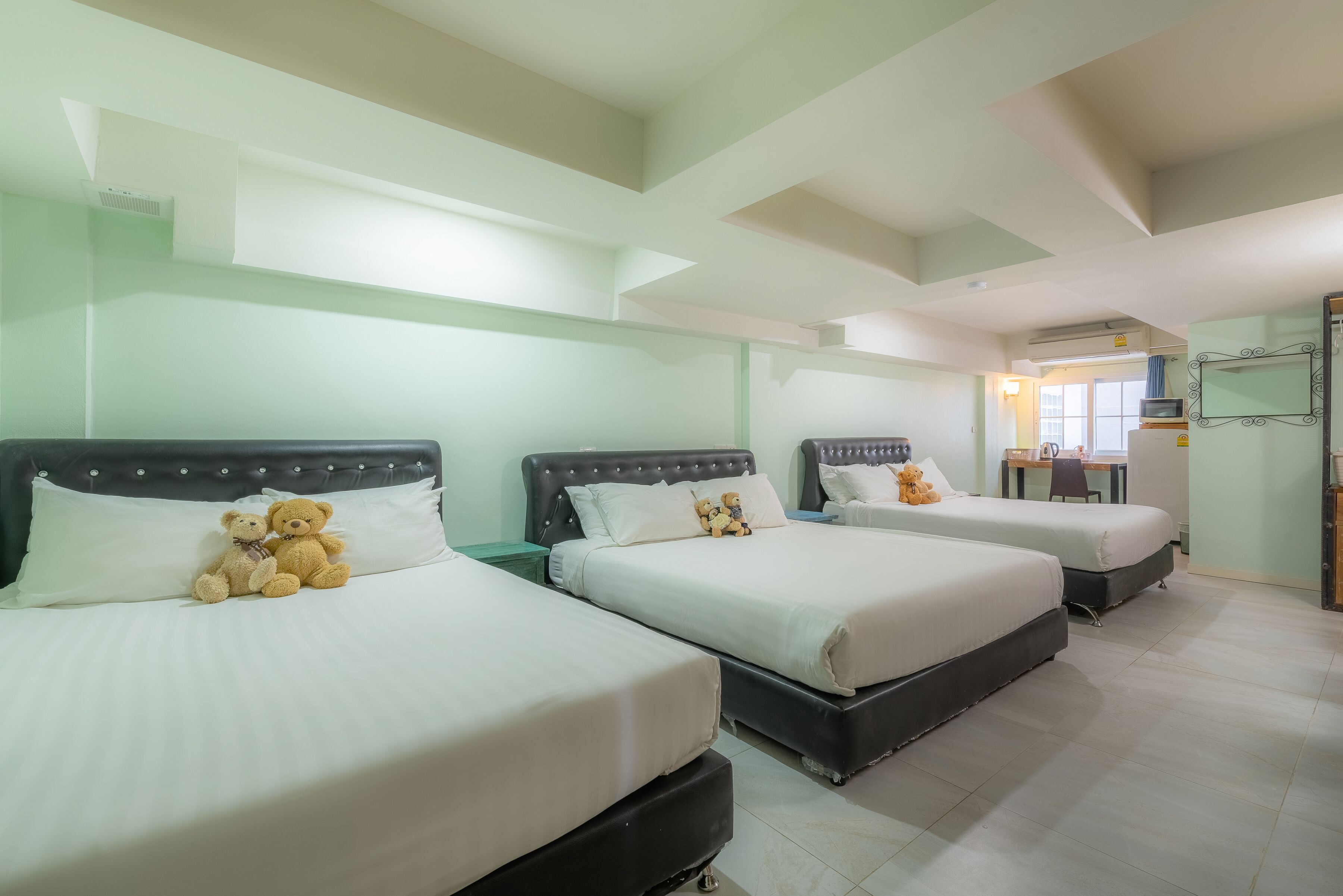 A hotel room with three beds, each with a headboard and white bedding. There are teddy bears on the beds.