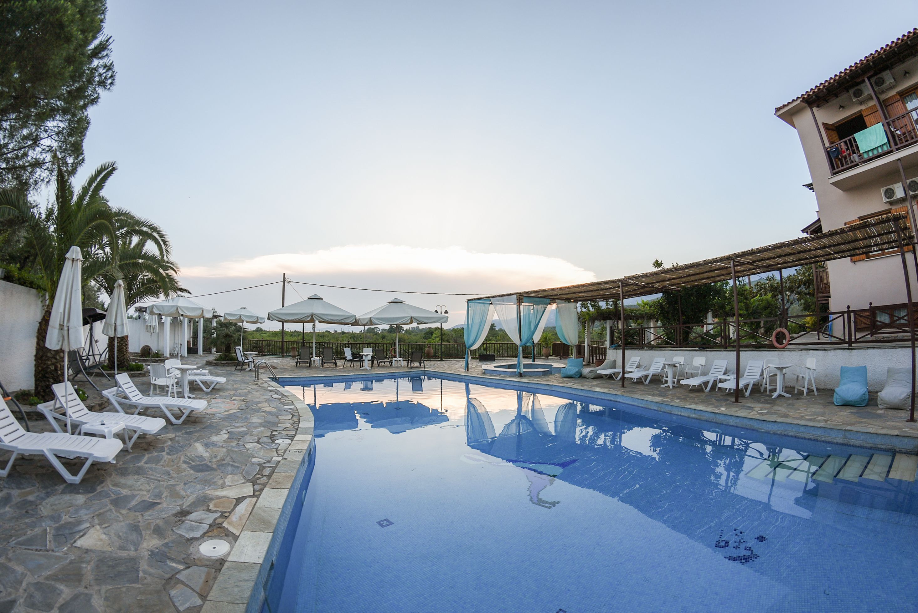 A swimming pool with lounge chairs and umbrellas, surrounded by stone flooring and a covered seating area.