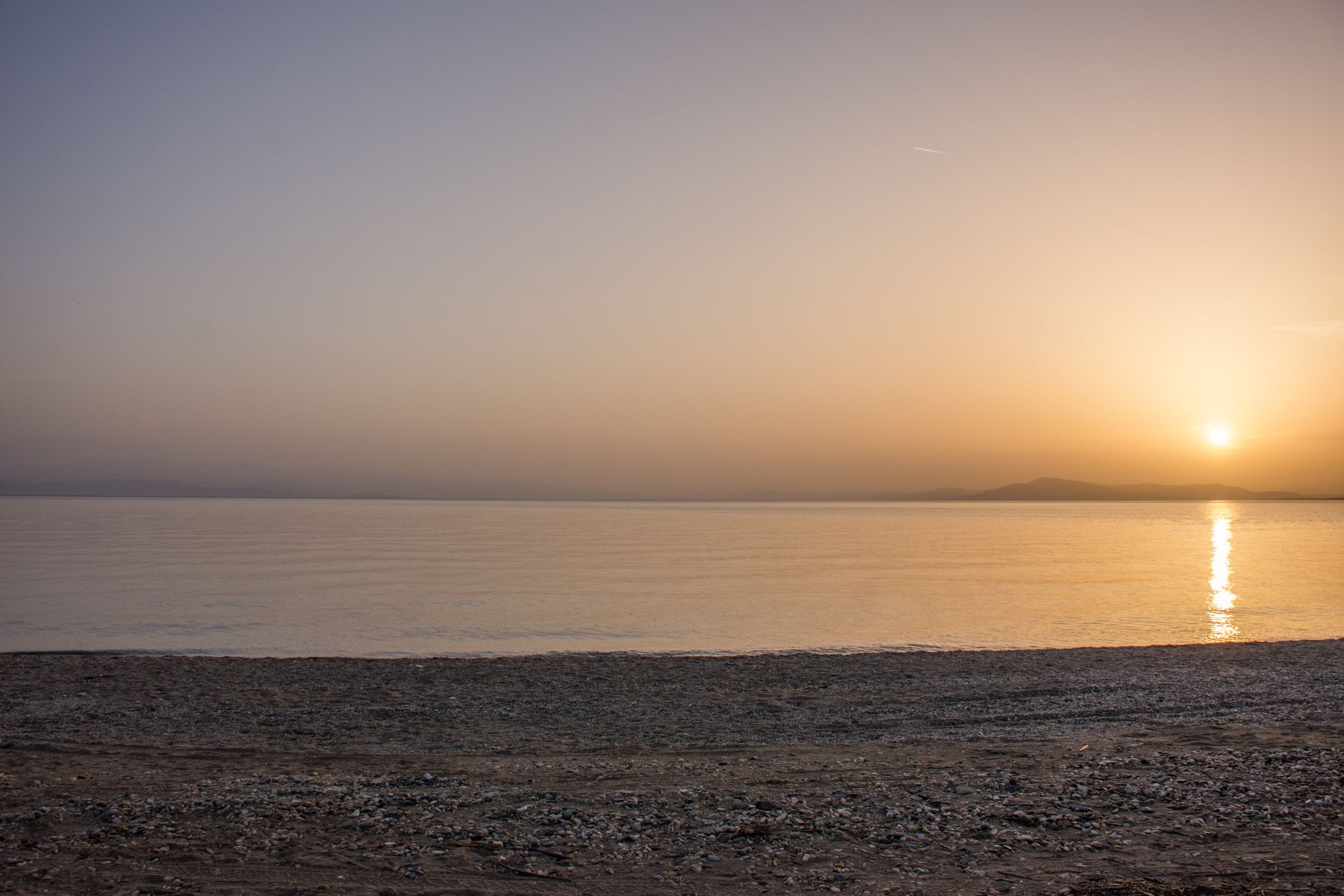 Una playa con un atardecer sobre el agua.