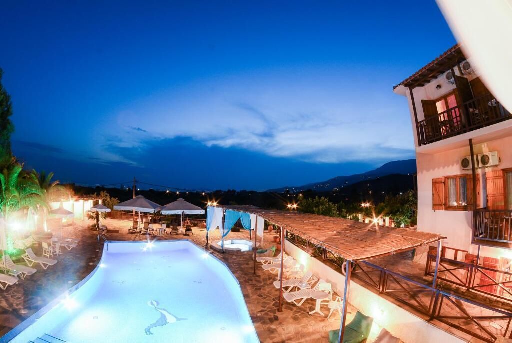 Un espace piscine avec des chaises longues et des parasols, un coin salon couvert et un bâtiment doté d’un balcon.