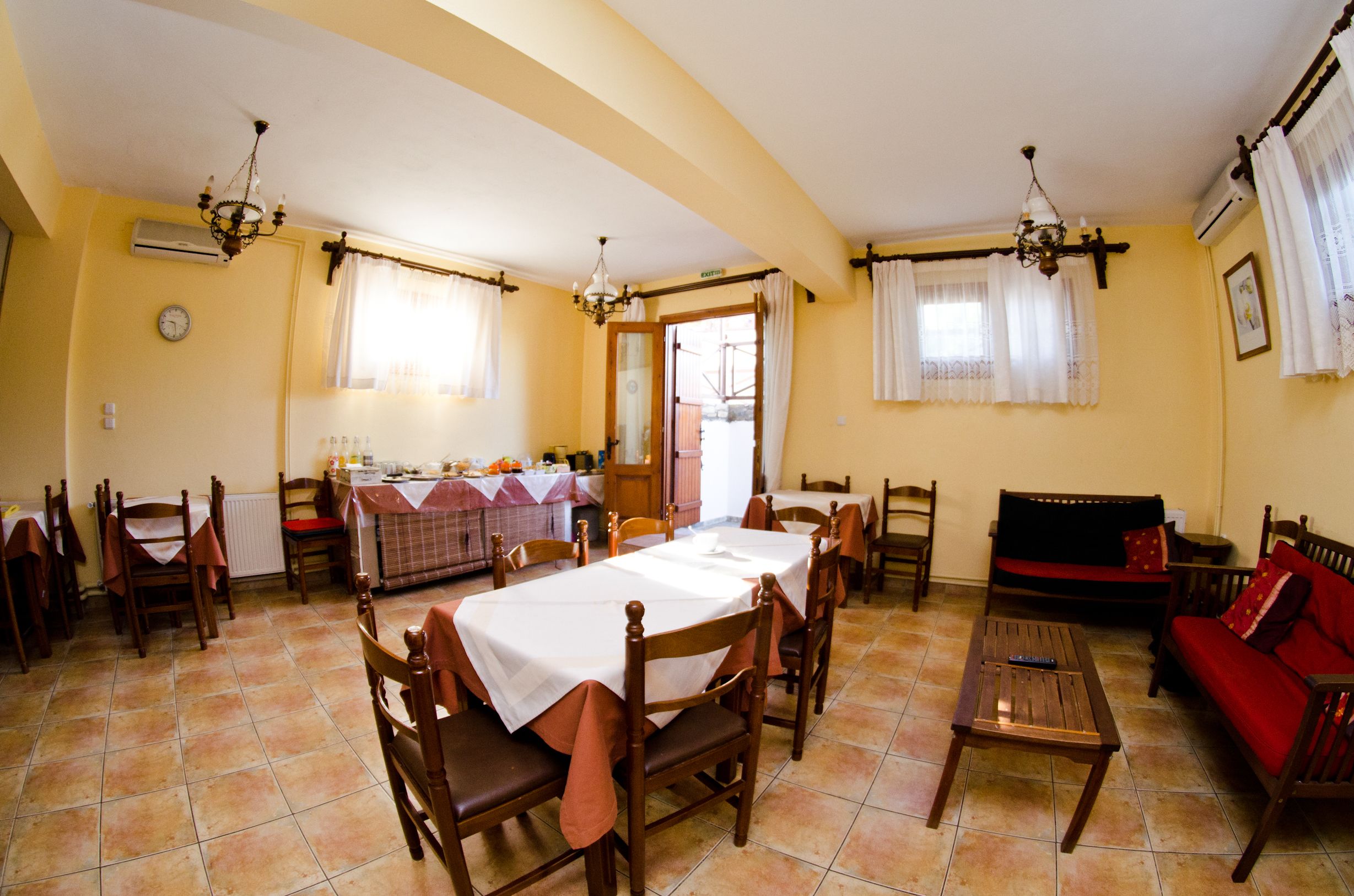 A dining area with a table set for four, surrounded by wooden chairs. There is a sofa and a small table with a remote control on it.