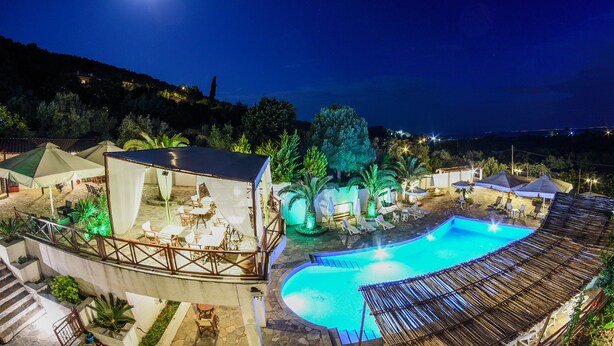 A nighttime view of a resort with a swimming pool, outdoor seating, and a covered area. - Seralis (South Pelion)